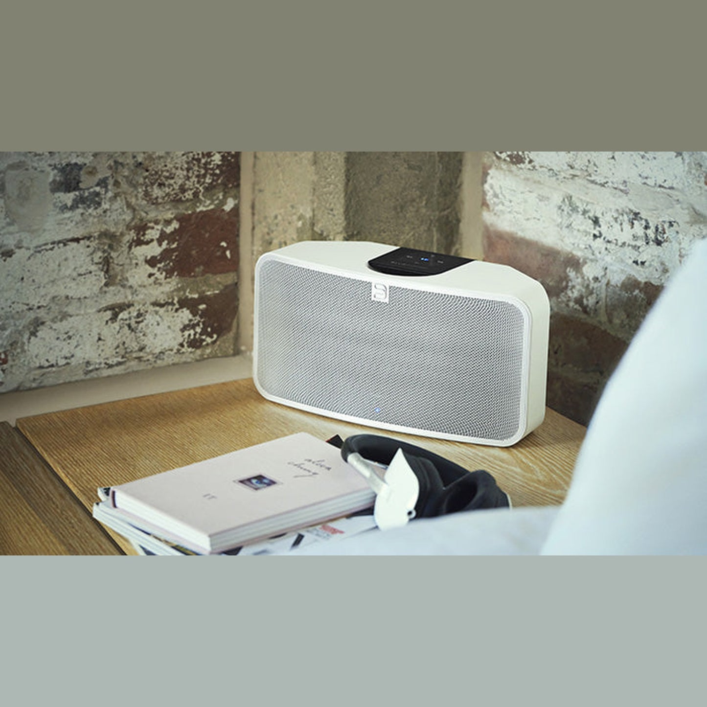 Bluesound Pulse Mini 2i Streaming-Lautsprecher Weiss Lifestyle auf Fensterbank vor Backsteinwand neben Buch