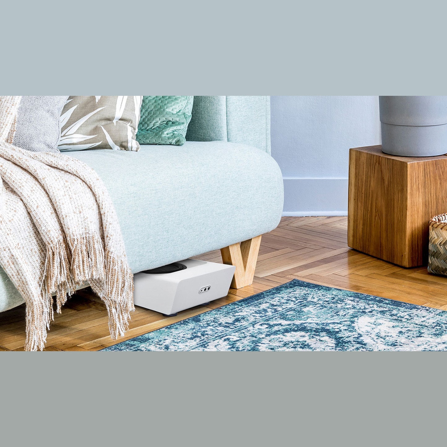 Bluesound Pulse Sub+ Subwoofer Weiss Lifestyle liegend unter dem Sofa im Wohnraum