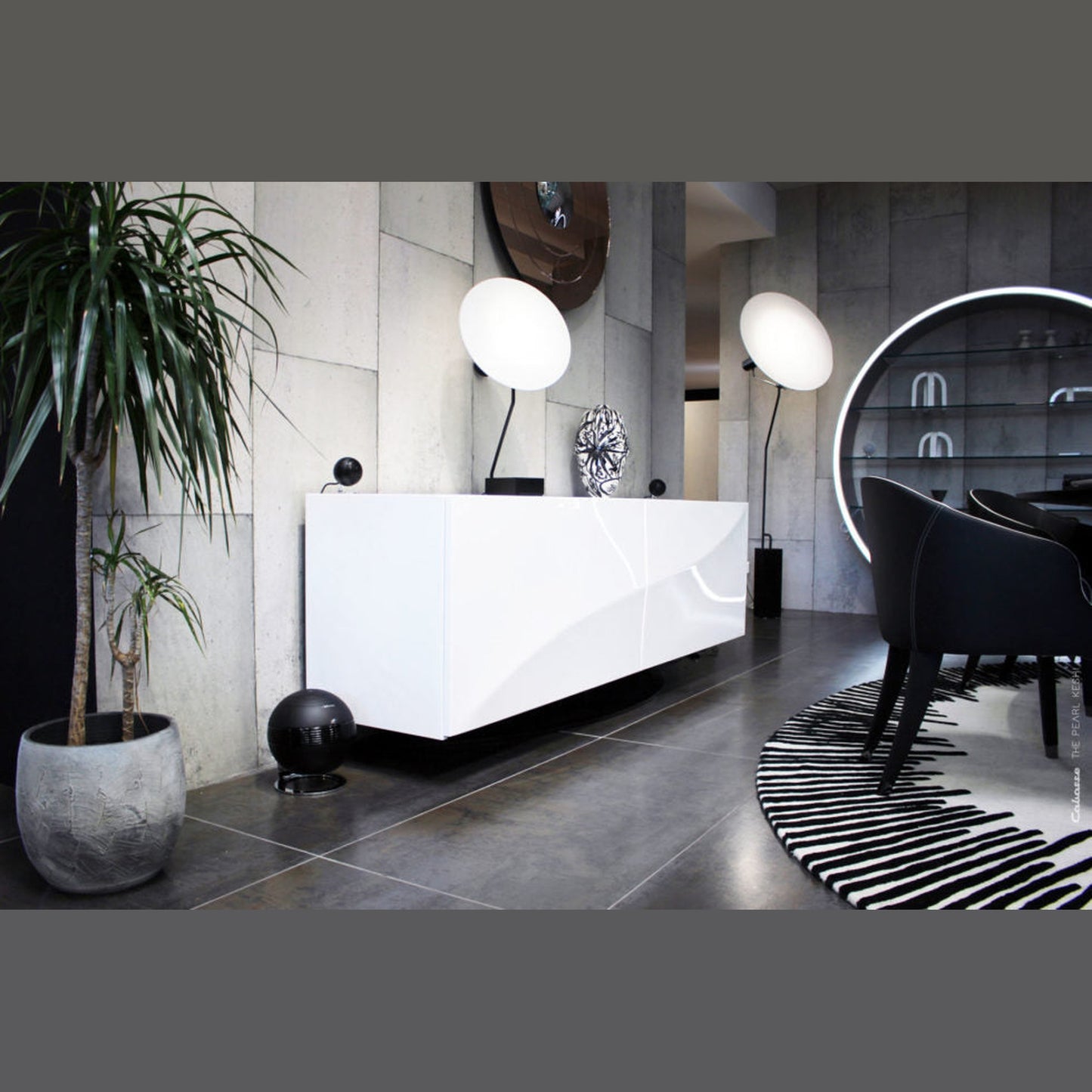Cabasse The Pearl Keshi 2.1-System Lifestyle in Schwarz, Subwoofer am Boden neben weissem Empfangstresen