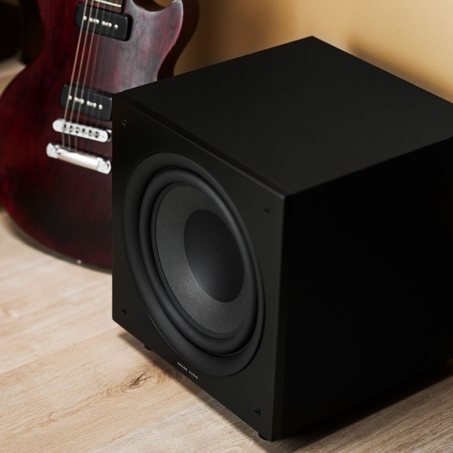 Argon Audio Malmö Sub 10 Aktiv-Subwoofer schwarz Lifestyle im Wohnraum neben E-Gitarre