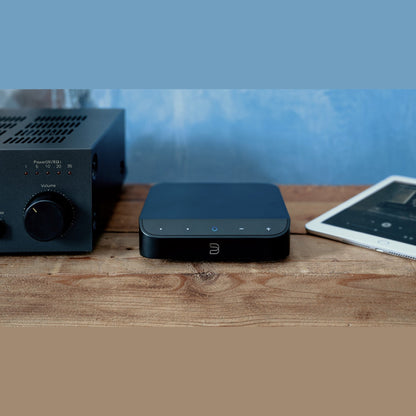 Bluesound Node Nano Netzwerk-Streamer Lifestyle auf Holzablage neben Verstärker und Tablet