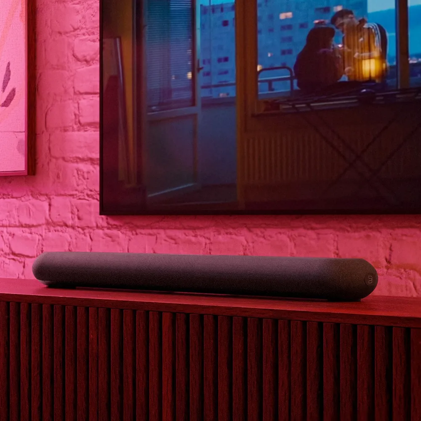 Bluesound Pulse Cinema Mini Soundbar Schwarz Lifestyle unter dem Fernseher vor Backsteinwand