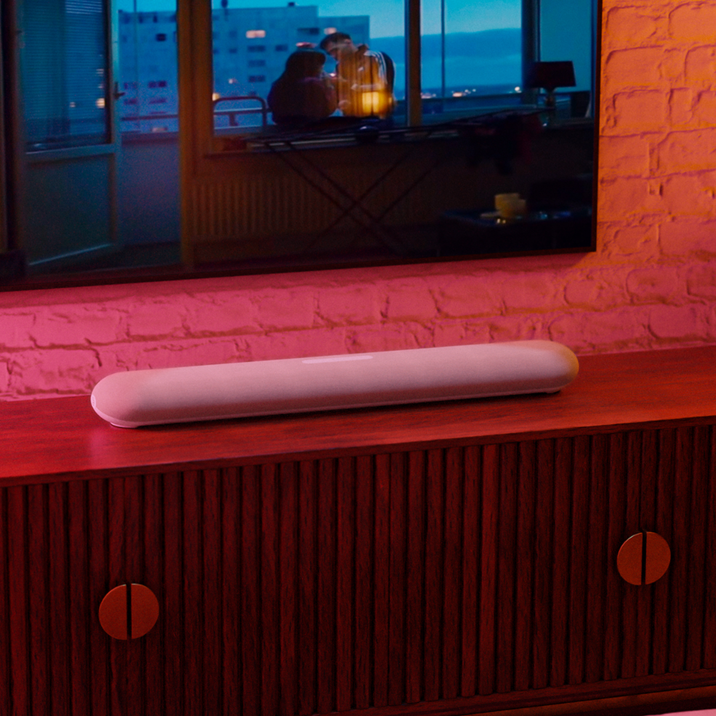 Bluesound Pulse Cinema Mini Soundbar Tan Lifestyle unter dem Fernseher bei farbigem Ambientelicht