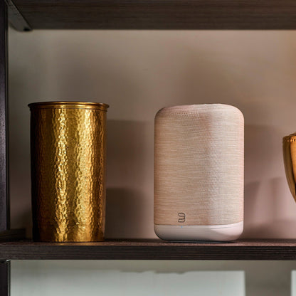 Bluesound Pulse Flex P130 Streaming-Lautsprecher Tan Lifestyle im Regal neben Messingvase
