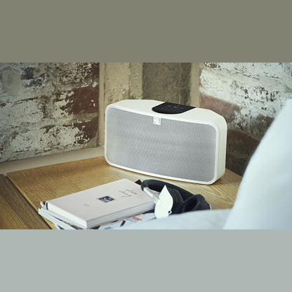 Bluesound Pulse Mini 2i Streaming-Lautsprecher Weiss Lifestyle auf Fensterbank vor Backsteinwand neben Buch