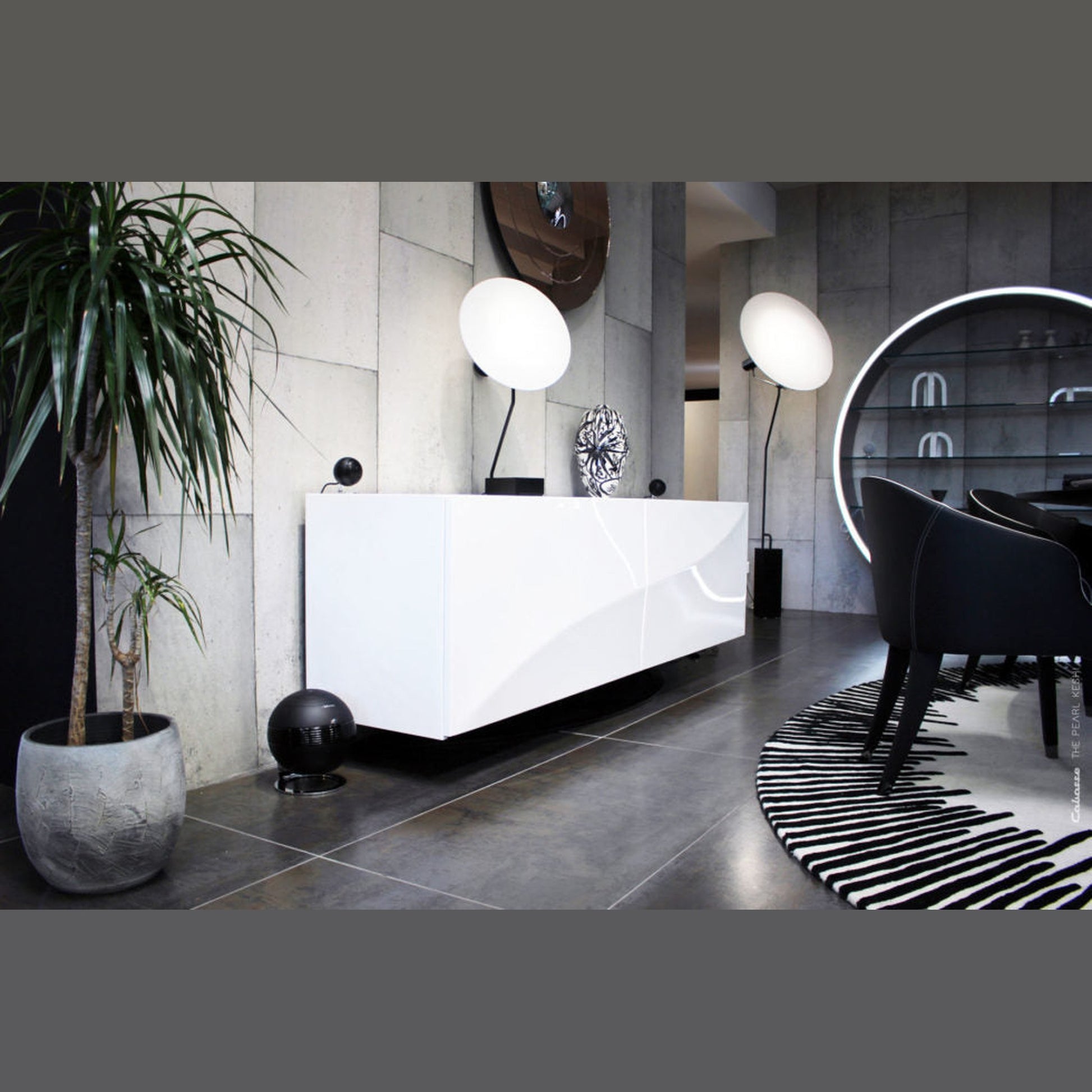 Cabasse The Pearl Keshi 2.1-System Lifestyle in Schwarz, Subwoofer am Boden neben weissem Empfangstresen