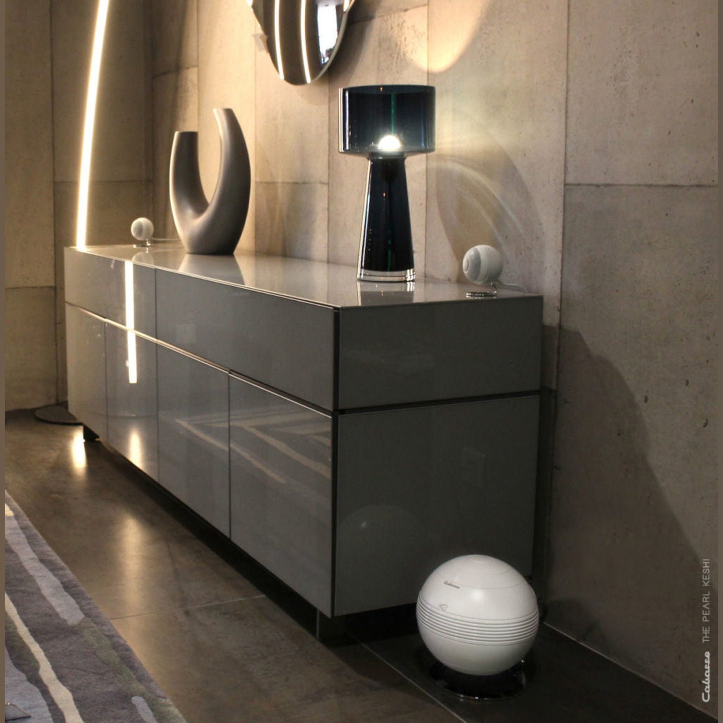 Cabasse The Pearl Keshi 2.1-System Lifestyle in Weiss neben grauem Hochglanz-Sideboard vor Betonwand