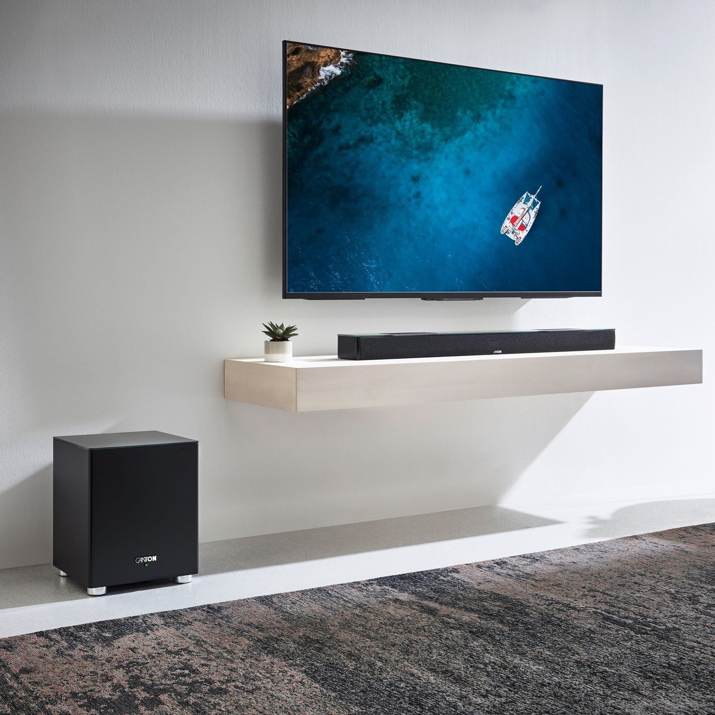 Canton Smart Soundbar 10 S2 Soundbar Schwarz Lifestyle auf Wandboard mit Fernseher und Subwoofer