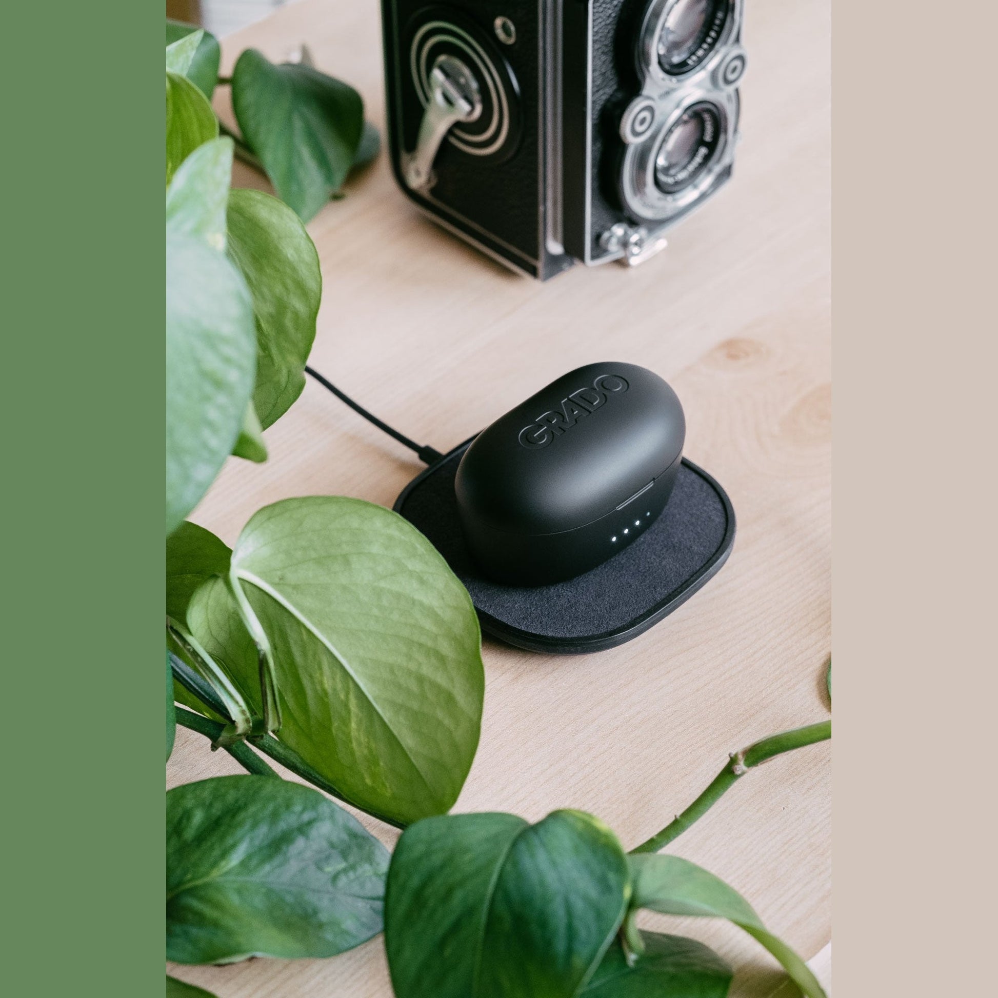 Grado GT220 True-Wireless-In-Ear-Kopfhörer Lifestyle geschlossene Ladebox auf einer Ladematte auf Holztisch