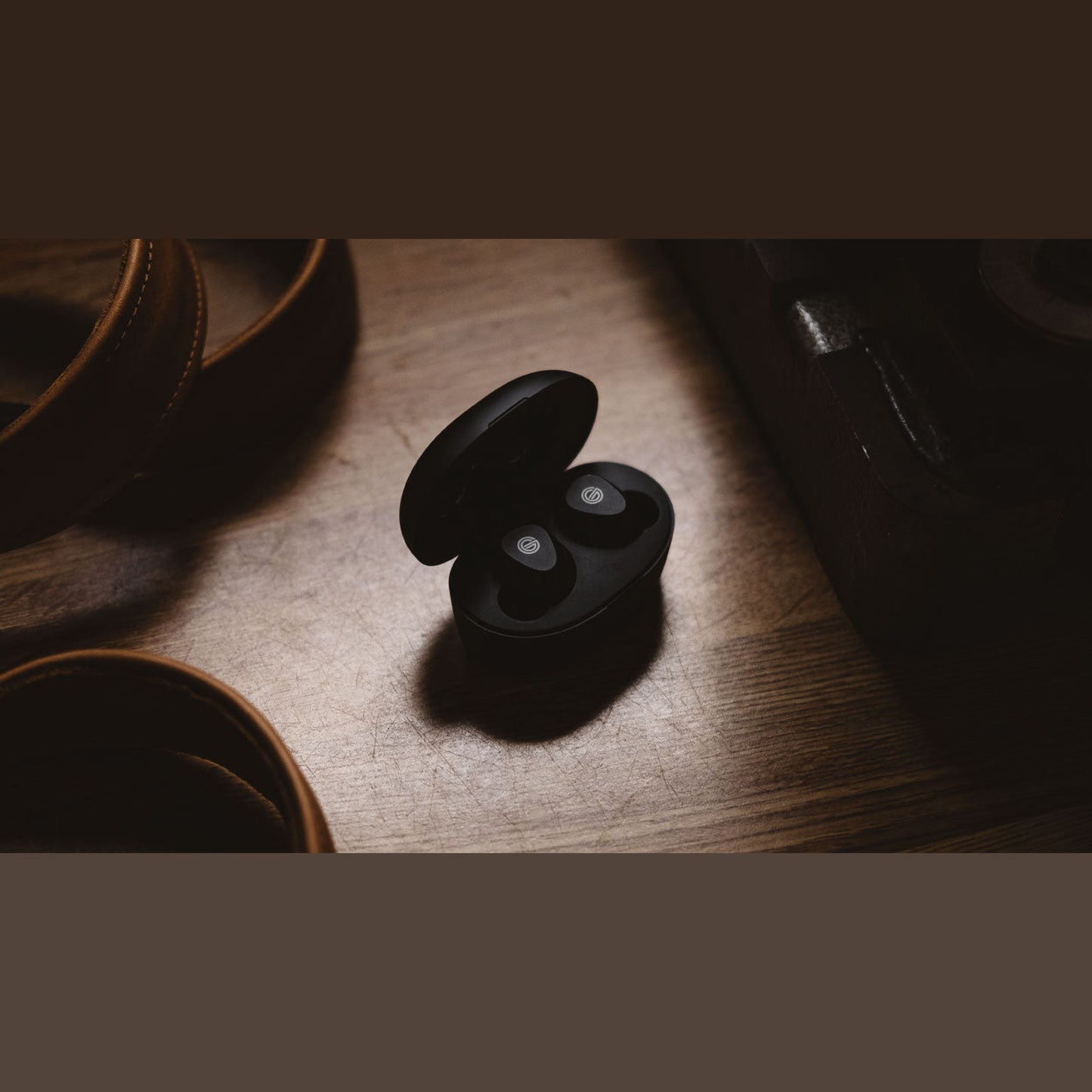 Grado GT220 True-Wireless-In-Ear-Kopfhörer Lifestyle geöffnete Ladebox auf Holztisch neben Lederriemen