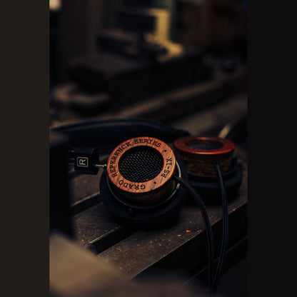Grado Reference RS1x Open-Back-Kopfhörer Lifestyle auf dunklem Maschinentisch neben rotem Holzring