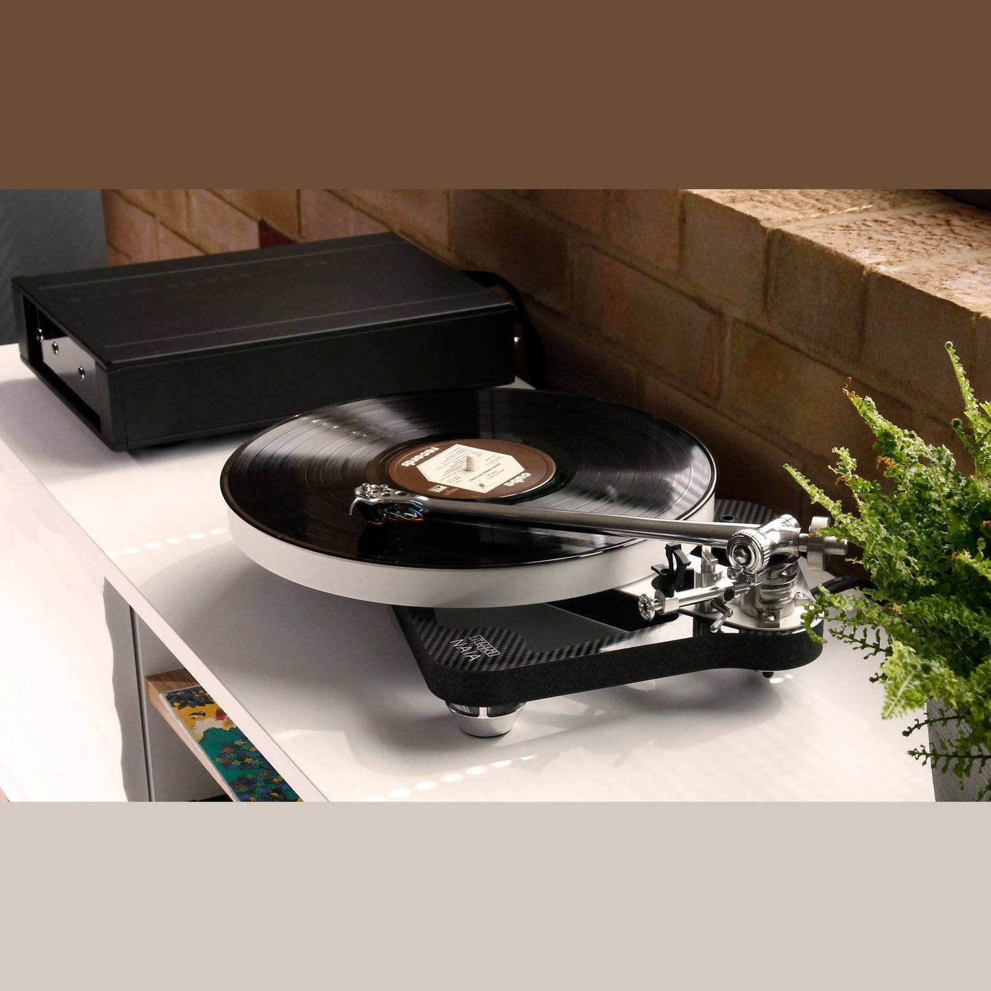 Rega Naia Plattenspieler mit Reference-Netzteil, Lifestyle-Ansicht auf Sideboard vor Backsteinwand