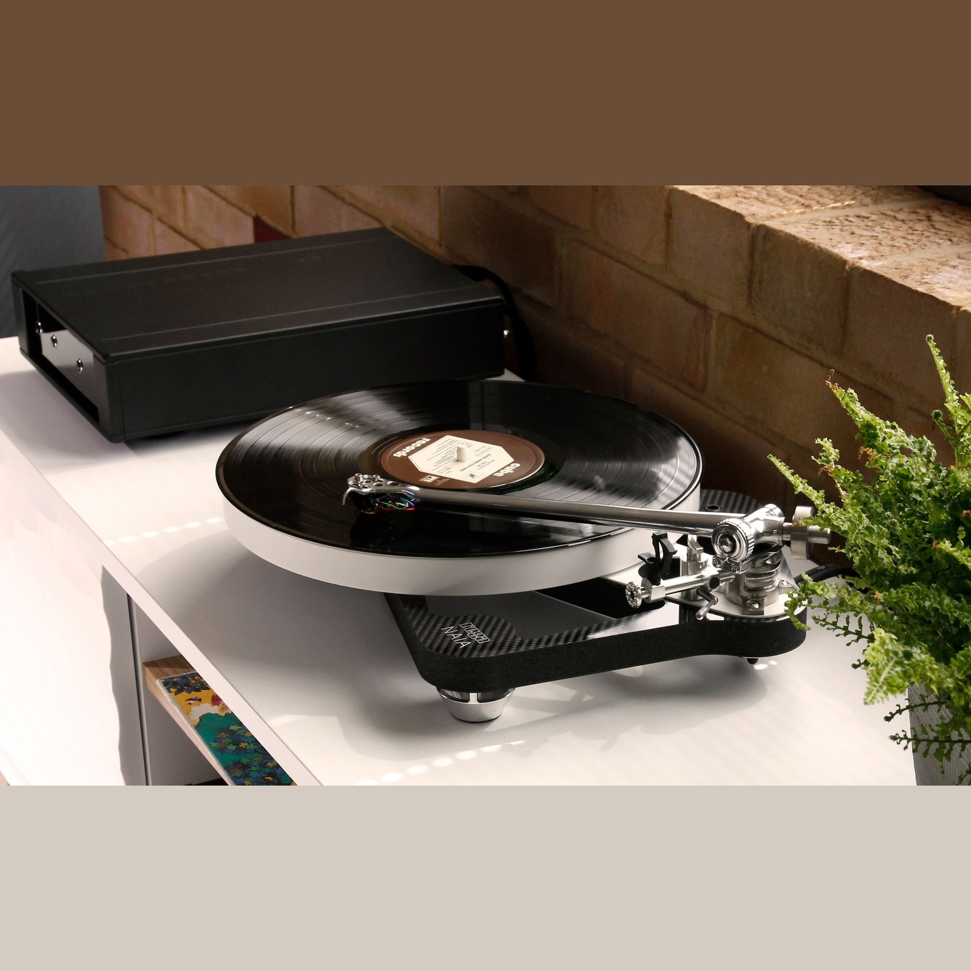 Rega Naia Plattenspieler mit Reference-Netzteil, Lifestyle-Ansicht auf Sideboard vor Backsteinwand