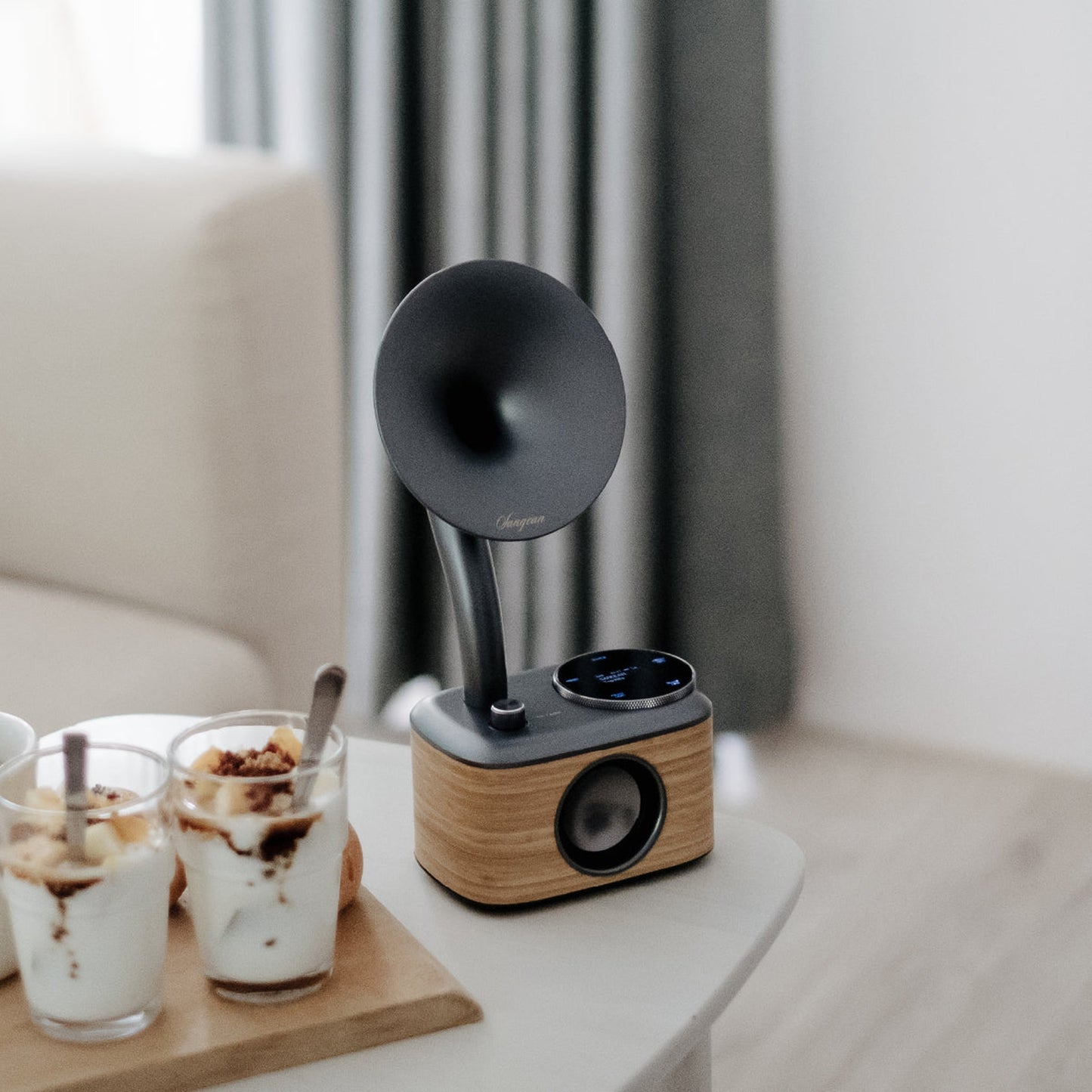 Sangean CP-100D DAB+/UKW Radio Lifestyle auf Beistelltisch neben Dessertgläsern in Lightwood-Grey
