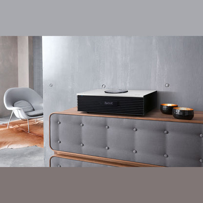 Technics SC-C70MK2 Kompaktanlage Silber Lifestyle auf Holzkommode vor Betonwand mit Sessel