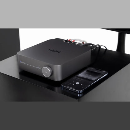 WiiM Amp Streaming-Verstärker Space Gray Lifestyle 3 auf dem Schreibtisch mit Smartphone